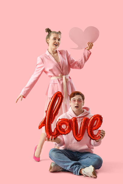 Νεαρό ζευγάρι με λευκή φούσκα ομιλίας και λέξη ΑΓΑΠΗ φτιαγμένη από μπαλόνια σε ροζ φόντο. Γιορτή του Αγίου Βαλεντίνου - Φωτογραφία, εικόνα