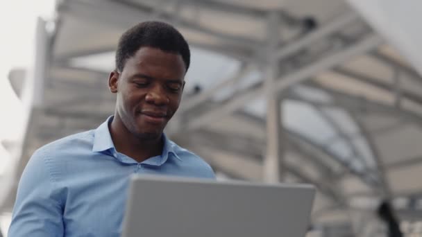 笑顔のアフリカ系アメリカ人ガイ 外からラップトップで作業. 屋外で座っている間オンラインで勉強するハンサムな多民族ビジネスマン. 人と技術コンセプト。 クローズアップ - 映像、動画