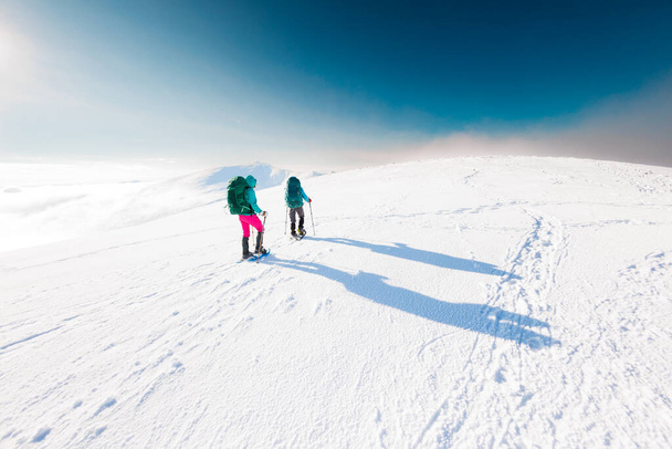 climbers climb the mountain. Winter mountaineering. two girls in snowshoes walk through the snow. hiking in the mountains in winter. - Photo, Image