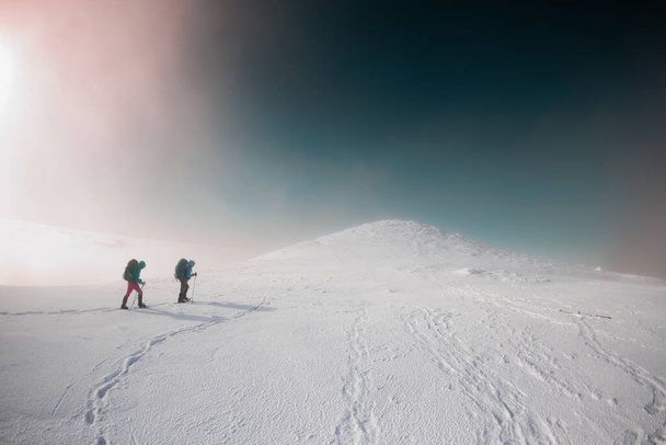 klimmers beklimmen de berg. Winterbergbeklimmen. twee meisjes in sneeuwschoenen lopen door de sneeuw. wandelen in de bergen in de winter. - Foto, afbeelding