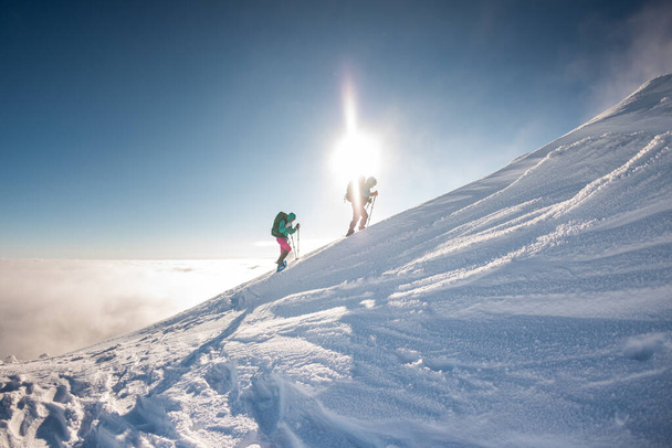 Zwei Bergsteiger erklimmen den Berg. Zwei Mädchen erklimmen einen schneebedeckten Berg. Winterbergsteigen. - Foto, Bild