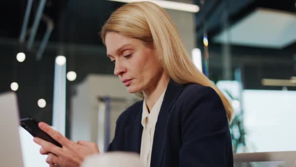Beautiful focused serious business woman in modern office using mobile phone texting messaging in corporate office building checking email messages online successful female executive at work. - Footage, Video