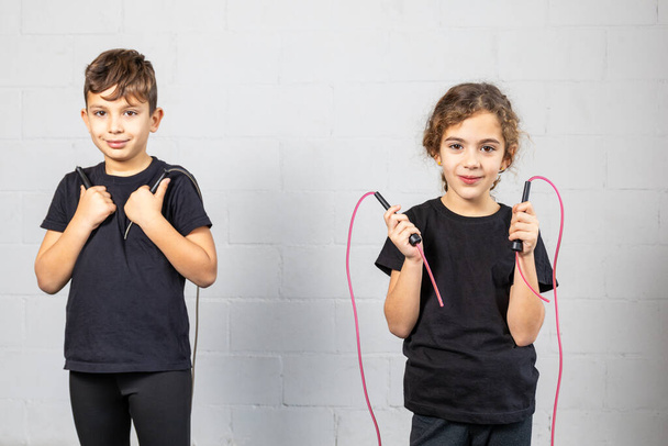 Горизонтальні фото елементарного хлопчика і дівчинки, одягнені в легінси і чорну футболку, зігріваються з мотузкою в спортзалі. Концепція спорту, відпочинок. - Фото, зображення