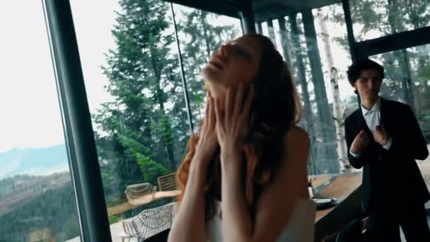Fairy-tale wedding couple posing in a stylish house with panoramic windows and mountain views. Red-haired bride posing with the groom. Wedding concept - Footage, Video