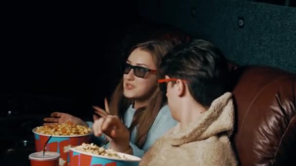 Coppia innamorata Un ragazzo e una ragazza mangiano popcorn e guardano un film in un cinema con occhiali 3D. Concetto di uno spettacolo cinematografico in un cinema - Filmati, video