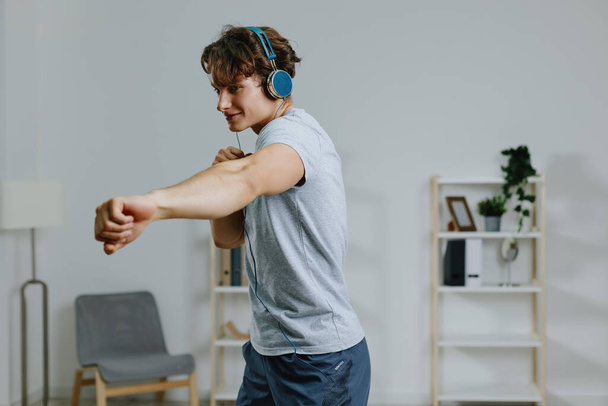 férfi beltéri fülhallgató technológia életmód padló edzés tevékenység fejhallgató tutorial otthon sport online szürke izom nyújtás illik egészséges ház tornaterem - Fotó, kép