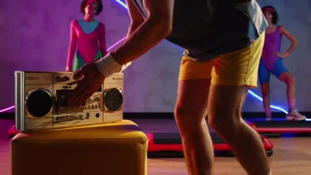 Colpo ritagliato di gruppo di persone che fanno aerobica riscaldandosi alla musica mentre il pullman carica cassetta a boombox in studio al neon - Filmati, video