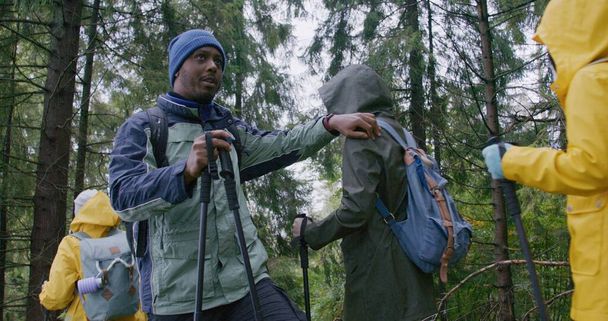 Afrikai amerikai túravezető megáll, hogy várjon egy csoport turistát, és beszél velük. A változatos túrázók hátizsákokkal és botokkal sétálnak az erdőben. Kültéri rajongók az expedíció alatt. Lassú mozgás.. - Fotó, kép