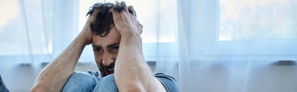 травмированный мужчина в повседневной футболке сидит на диване и кричит, психическое здоровье осведомленности, баннер - Фото, изображение