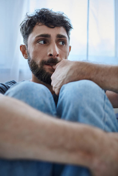 traumatyczny niespokojny mężczyzna w luźnych ubraniach, siedzący na kanapie podczas załamania, świadomość zdrowia psychicznego - Zdjęcie, obraz