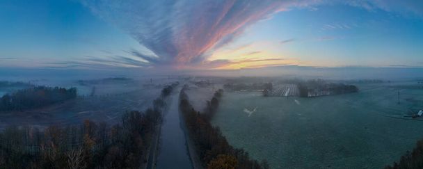 An expansive panorama unfolds in this aerial photograph, where a new days light gently graces a pastoral landscape. A central river or waterway cuts through the frame, leading the eye toward the - Photo, Image