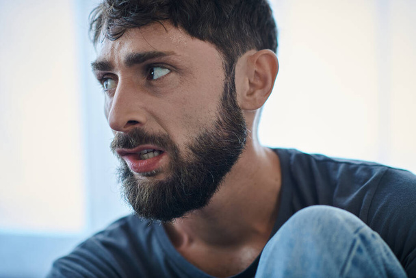 homem mal traumatizado com barba mordendo os lábios durante episódio depressivo, consciência de saúde mental - Foto, Imagem