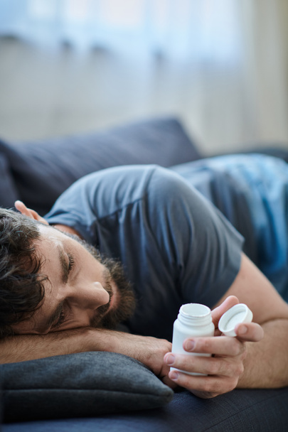 traumatizovaný trpící muž s vousy ležící na pohovce s pilulkami v ruce, duševní zdraví vědomí - Fotografie, Obrázek