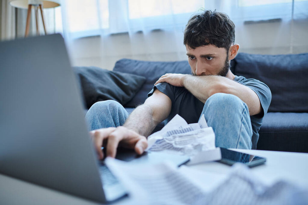 καταθλιπτικός άντρας με γενειάδα σε περιστασιακή ενδυμασία κοιτάζοντας το laptop του κατά την κατάρρευση, ψυχική υγεία - Φωτογραφία, εικόνα