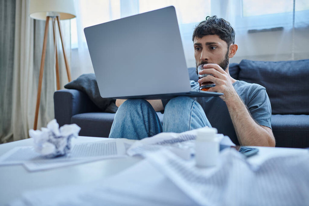 kétségbeesett traumatizált férfi szakállas dolgozik laptop és iszik alkoholt az asztalon - Fotó, kép