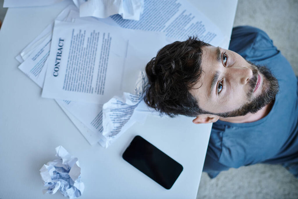 вид сверху депрессивный человек со смартфоном с бумагами и контракт рядом с ним во время психического срыва - Фото, изображение