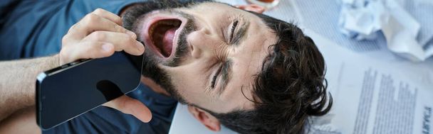 απογοητευμένος άντρας να ουρλιάζει στο τηλέφωνο με ένα ποτήρι αλκοόλ δίπλα του κατά τη διάρκεια της ψυχικής κατάρρευσης, πανό - Φωτογραφία, εικόνα