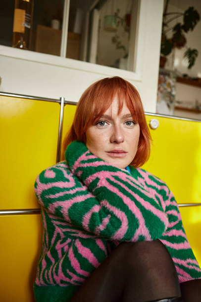 Nachdenkliche Frau im stylischen Animal-Print-Pullover sitzt in Wohnung in Wien und blickt in die Kamera - Foto, Bild