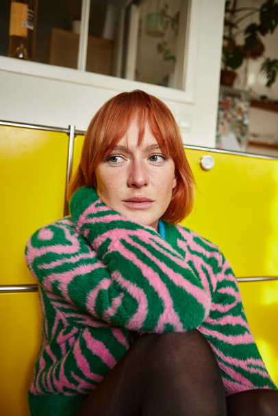 Nachdenkliche Frau im Animal-Print-Pullover sitzt in moderner Wohnung in Wien und schaut weg - Foto, Bild