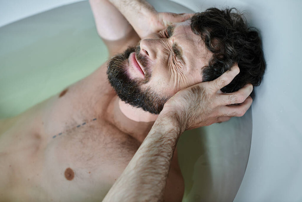 άρρωστος τραυματισμένος άνδρας με γενειάδα ξαπλωμένος στην μπανιέρα του κατά τη διάρκεια της κατάρρευσης, συνειδητοποίηση της ψυχικής υγείας - Φωτογραφία, εικόνα