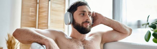 fröhlicher gutaussehender Mann mit Kopfhörern, der in seiner Badewanne sitzt und entspannt, geistige Gesundheit, Banner - Foto, Bild