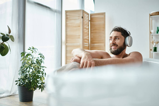 joyful attractive man with beard and headphones sitting and relaxing in his bathtub, mental health - Foto, afbeelding