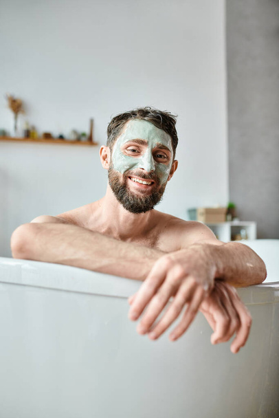 joyful attractive man with beard and face mask chilling in his bathtub, mental health awareness - Photo, Image