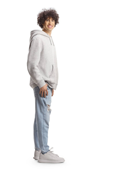 Full length portret van een schattige lange man met krullend haar in een grijze hoodie en jeans geïsoleerd op witte achtergrond - Foto, afbeelding