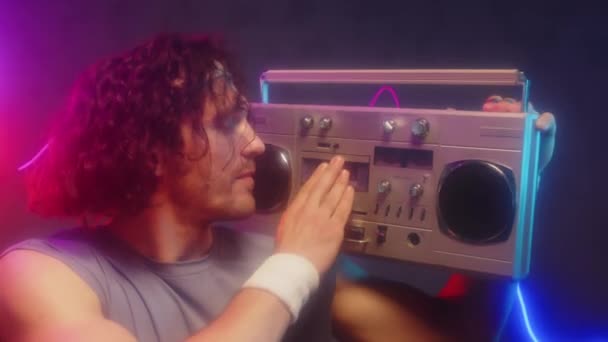 Medium close up portrait of cheerful young male adult turning on boombox with cassette and looking at camera, 80s style - Footage, Video
