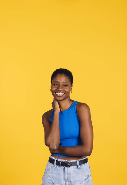 Portret van een vrolijke jonge mooie vrouw met blauwe kleren tegen een gele achtergrond. Jonge vrouw kijkt naar de camera. - Foto, afbeelding