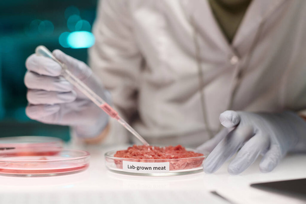 Ricercatore irriconoscibile che lavora su campioni di carne coltivati in laboratorio aggiungendo liquido usando pipetta - Foto, immagini