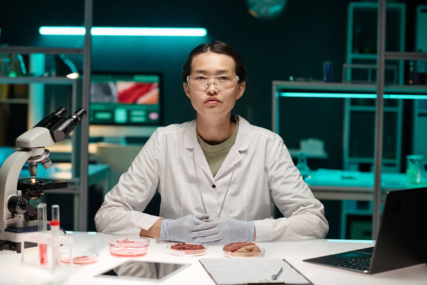 Junge asiatische Laborangestellte sitzt an ihrem Arbeitsplatz im Labor und schaut in die Kamera - Foto, Bild