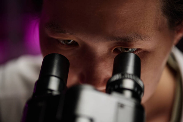 Primo piano estremo di occhi di ricercatore asiatico attentamente guardando attraverso il microscopio - Foto, immagini