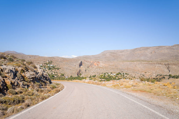 Cette photo de paysage a été prise, en Europe, en Grèce, en Crète, à Kato Zakros, Au bord de la mer Méditerranée, en été. Nous voyons une route asphaltée au milieu des montagnes arides et rocheuses, sous le soleil. - Photo, image