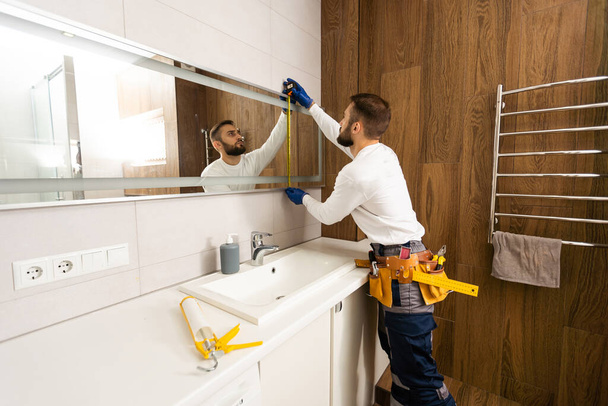 De werknemer installeert de spiegel in de badkamer - Foto, afbeelding