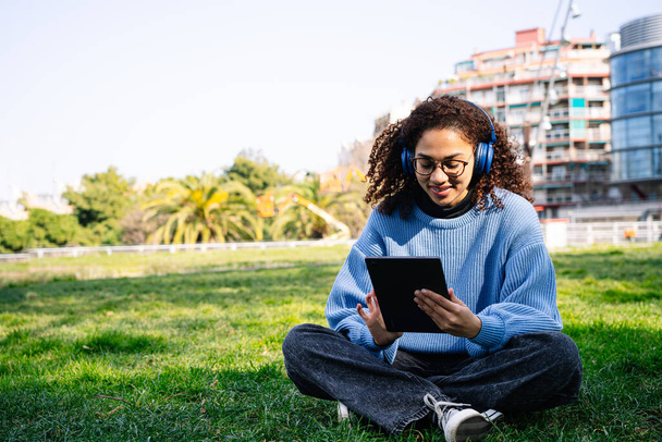 Zadowolenie młoda kobieta cieszy się cyfrowym tabletem pośród zieleni parku miejskiego. - Zdjęcie, obraz