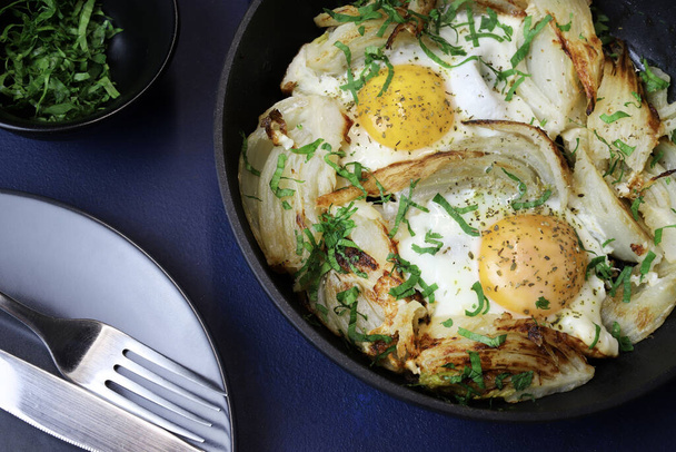 Zelfgebakken gebakken eieren en venkel met kruid in een ijzeren pan op donkere achtergrond. Gezond en vegetarisch voedsel. Bovenaanzicht. - Foto, afbeelding