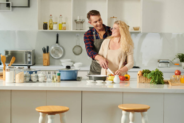 Радостная пара наслаждается романтическим свиданием на кухне, они флиртуют и готовят ужин - Фото, изображение