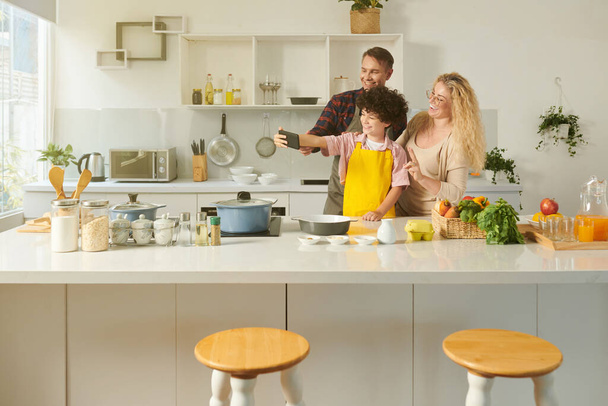 Радостный подросток делает селфи с родителями, когда они готовят вместе - Фото, изображение