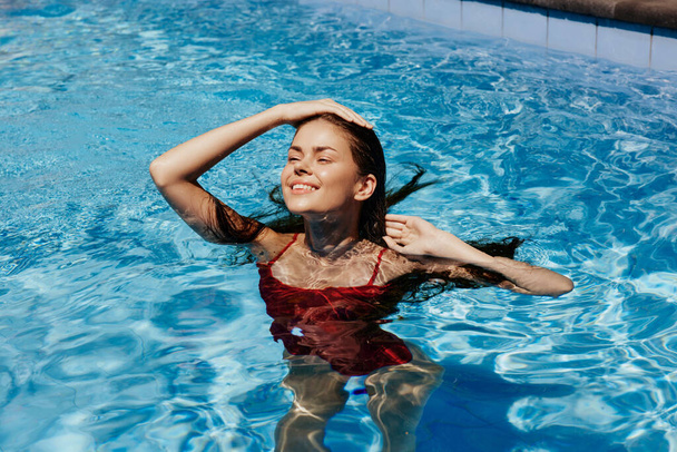 ハッピーな女性は,太陽の下でゆったりとした長髪の赤い水着でプールで泳ぎ,日焼け止め付きの肌の保護,熱帯気候での休暇でリラックスするというコンセプト. 高品質の写真 - 写真・画像