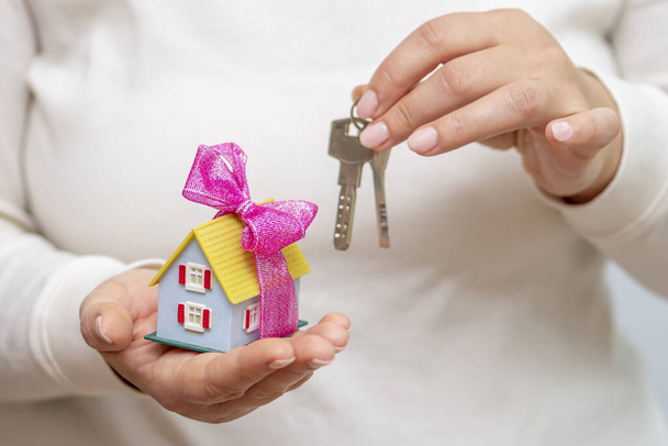 Female hands holding a bunch of keys and a toy house, light background. - Photo, Image