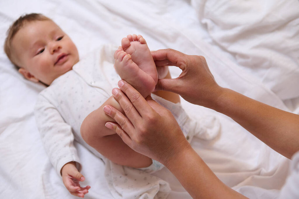 Bulanık, sevimli bir çocuğun annesinin elinde küçücük parmakları olan, annesine sarılarak gülümseyen küçük ayakların yakın çekimi. Bebeklik ve bebeklik. Doğumhane. Annelik ve bebek bakımı kavramı - Fotoğraf, Görsel