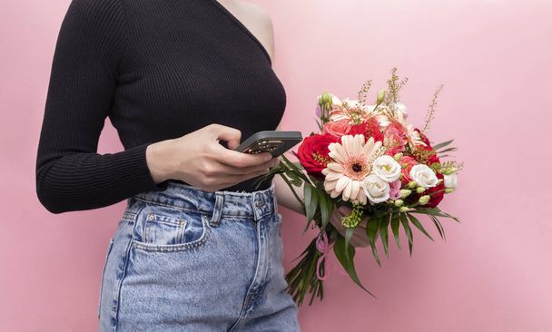 Fiatal kaukázusi nő Denim tartja telefon csokor friss virág rózsa, Gerbera, krizantém rózsaszín háttér. Online rendelés és a virág szállítási koncepció. Vízszintes sík. - Fotó, kép