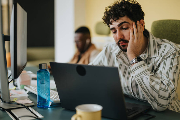 Schöne männliche Person starrt auf seinen Laptop, während er ringt, eine Lösung für sein Problem bei der Arbeit zu finden. - Foto, Bild