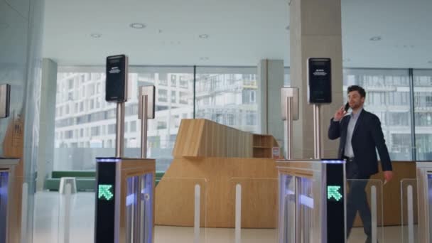 Businessman passing security entrance modern office talking smartphone. Elegant man ceo swiping card at turnstile electronic card reader. Smiling manager calling entering safety gates business center - Footage, Video