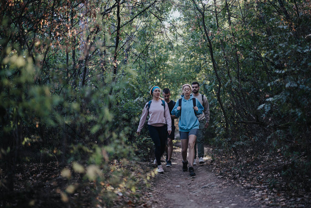 Los excursionistas felices disfrutan de un día libre de otoño en el bosque, haciendo ejercicio, explorando y teniendo conversaciones divertidas en medio de la belleza de la naturaleza. Una escapada de fin de semana perfecta con amigos en un paisaje verde y sereno. - Foto, imagen