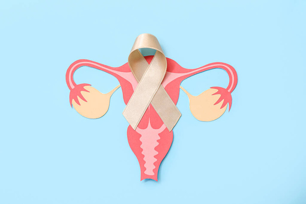 Beige ribbon with paper uterus on blue background. Cancer awareness concept - Photo, Image