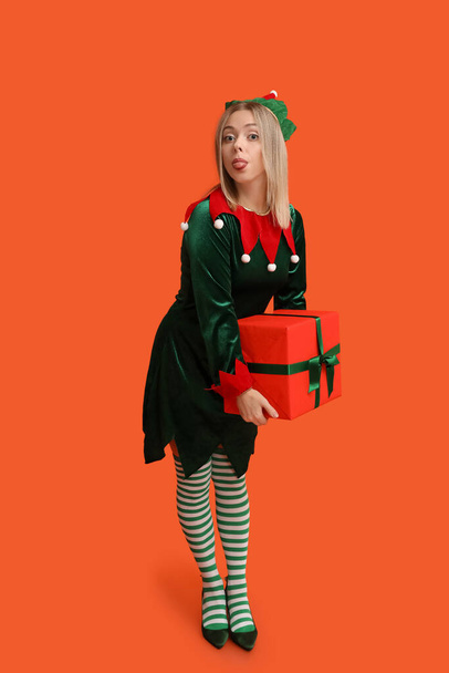 Young woman in elf costume with Christmas gift box on orange background - Photo, Image
