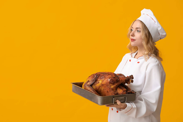 Young female chef with tasty baked turkey on yellow background. Thanksgiving Day celebration - Photo, Image