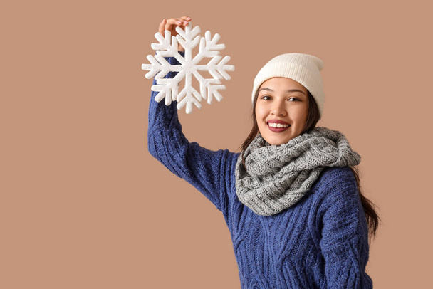 Hermosa mujer asiática joven en bufanda caliente con copo de nieve sobre fondo marrón - Foto, imagen